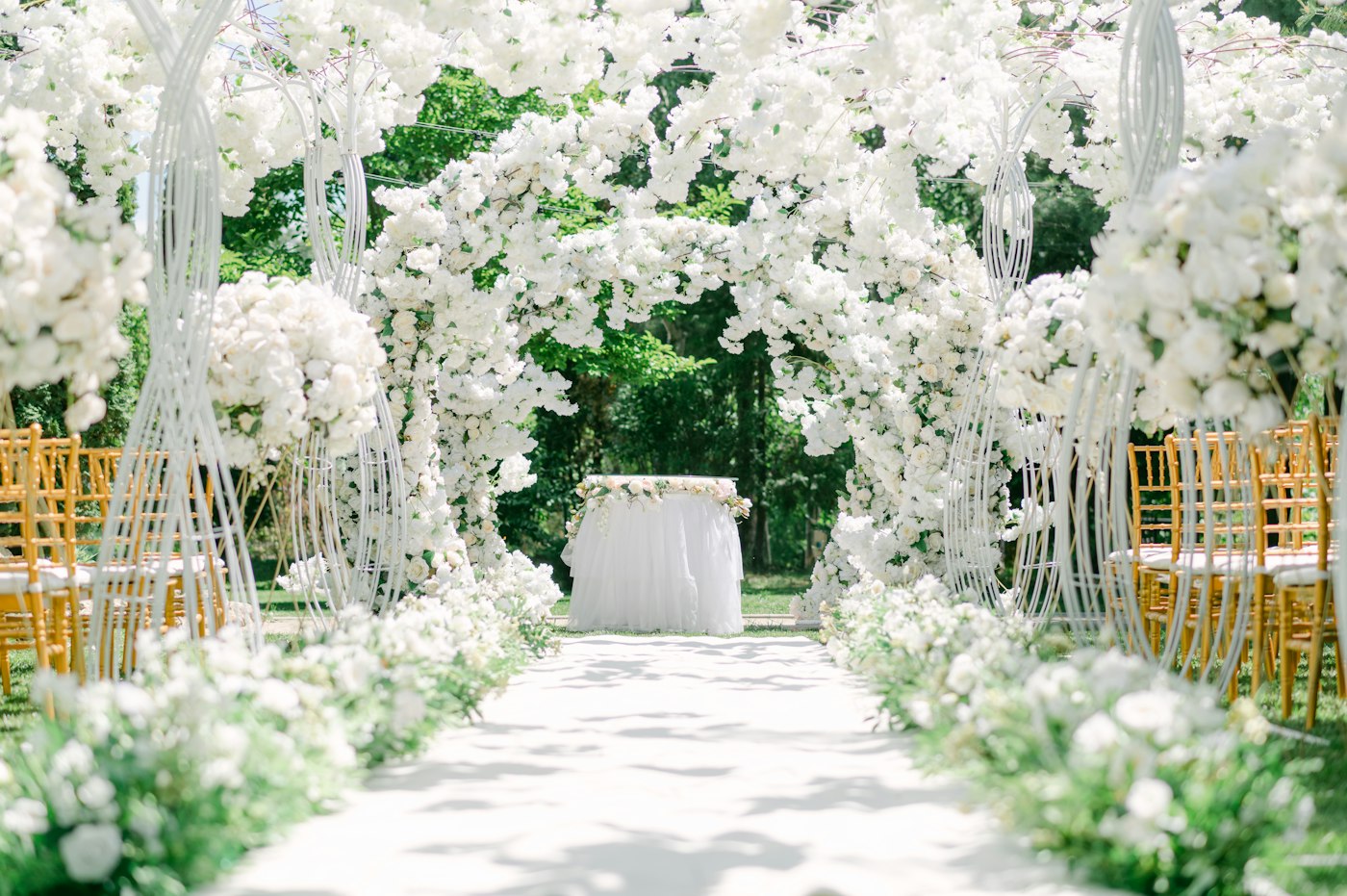 Hvit blomsterbue over en sti med gylne stoler, dekorert til bryllupsseremoni